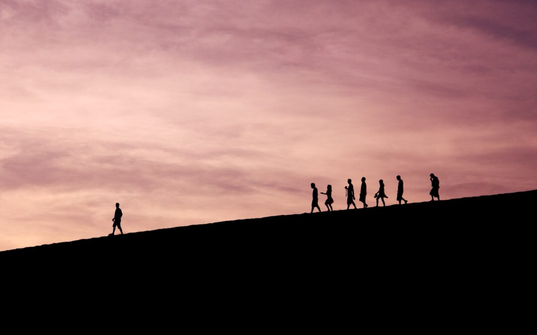Silhouette of one person leading a group of others down a mountain