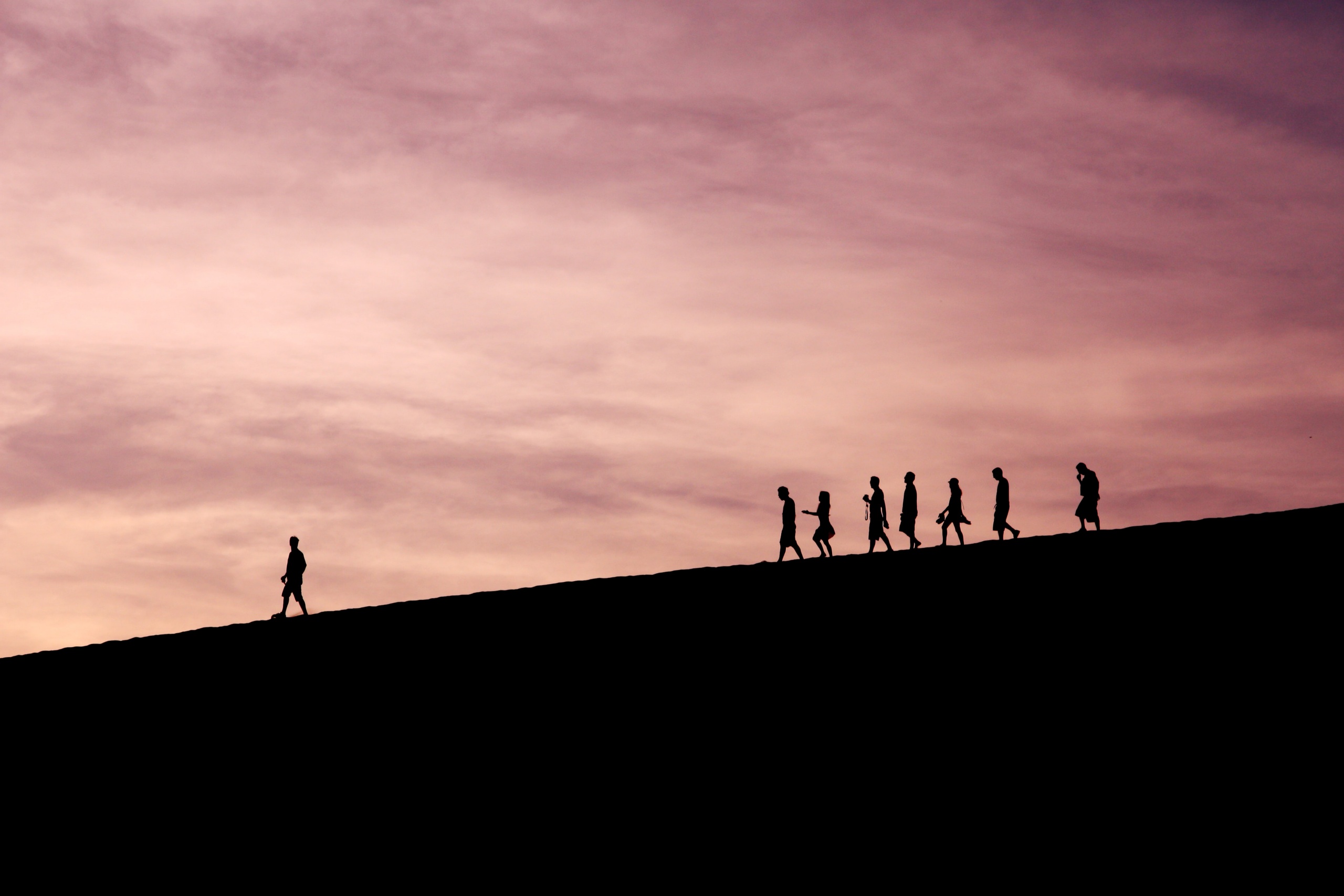 Silhouette of one person leading a group of others down a mountain