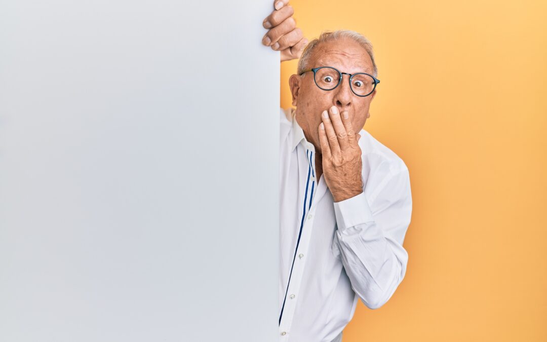 Man peeking around a wall with a surprised look on his face and a hand over his mouth