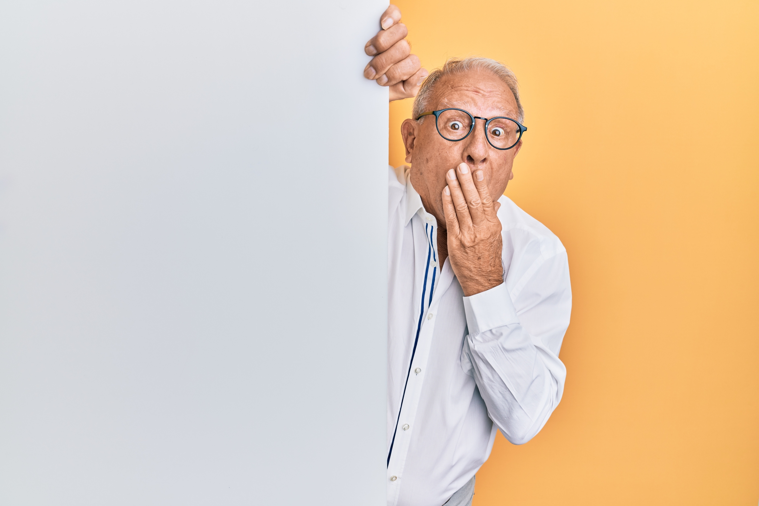 Man peeking around a wall with a surprised look on his face and a hand over his mouth