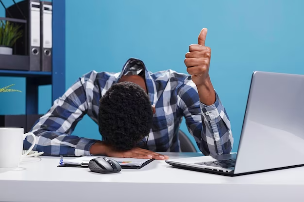 Exhausted young man with his head resting on his laptop keyboard, giving the thumbs up