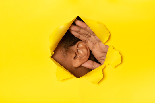 Someone listening through a hole in a yellow piece of paper