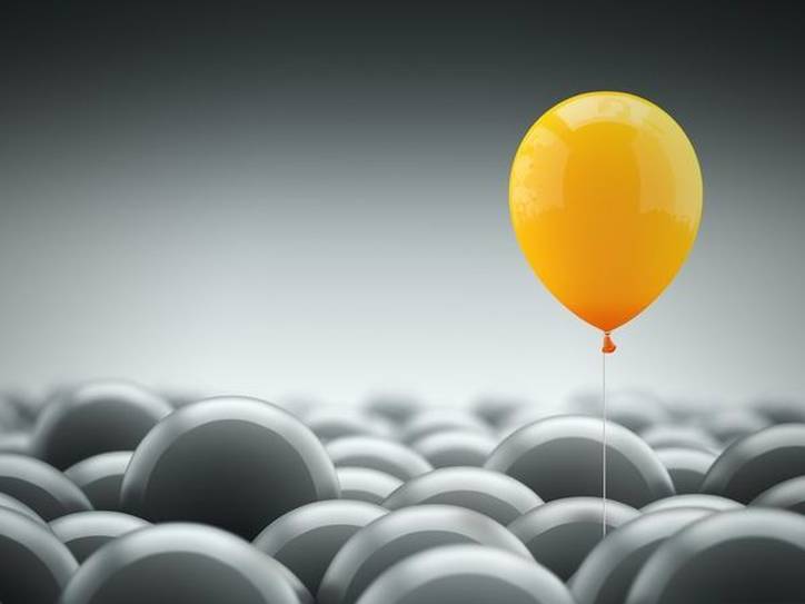 A yellow balloon floats above a sea of gray balloons