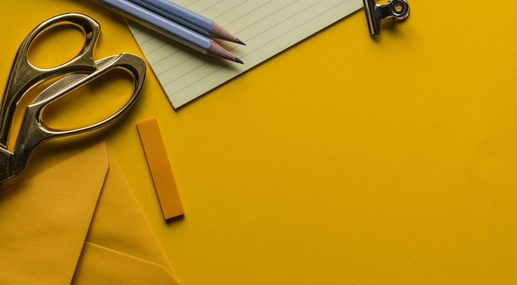Yellow desk with paper, pens, and scissors on it